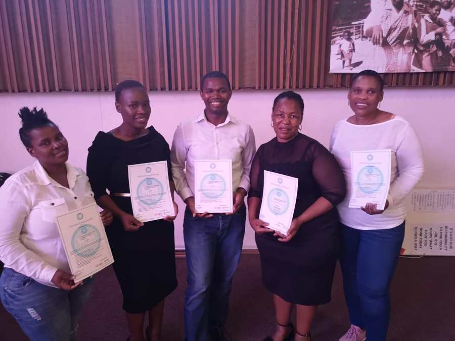 Five Izenzo Job Club members standing together holding their Certificates of Excellence at a graduation.