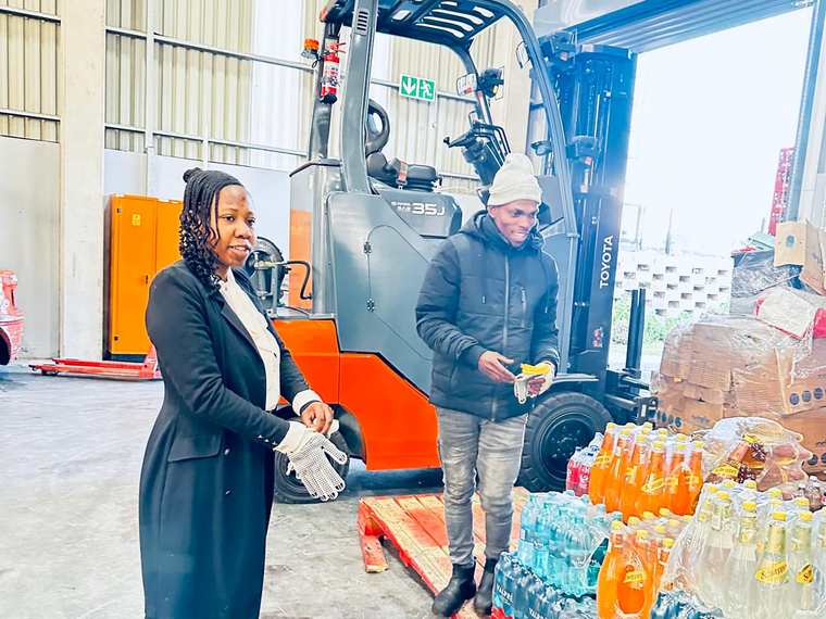 An Izenzo member in work gloves on the floor of a beverage distribution warehouse, beside a forklift and pallets of stock.