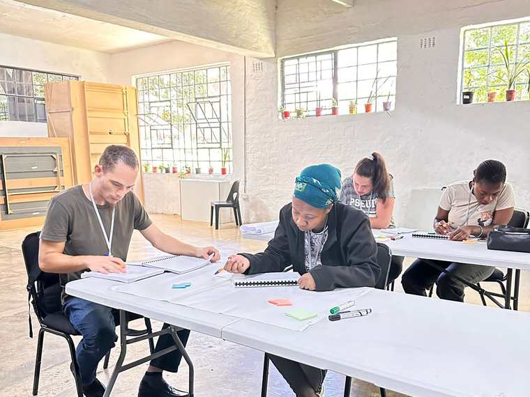 Members of the job club seated at tables in a bright workshop room, working through their notebooks.
